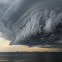 A mean looking huge storm cloud hovering over the ocean.