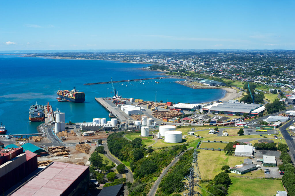 A view of the port of New Plymouth New Zealand with a container ship docking and one at the dock.